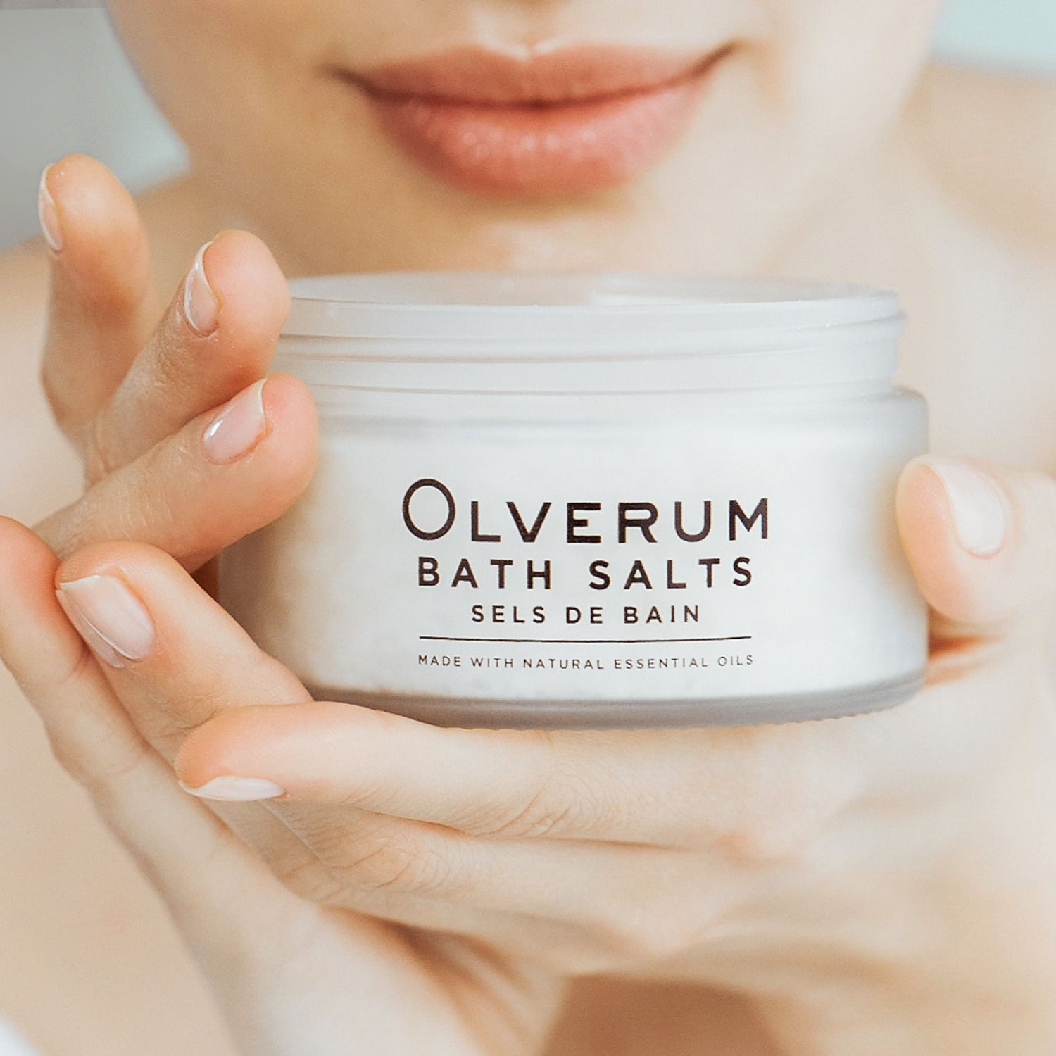 Olverum-bath-salts-being-held-in-hands-with-face-in-back-ground smelling