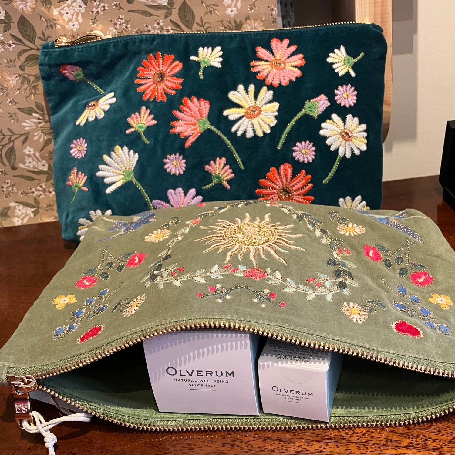one-teal-velvet-pouch-with-embroidered-flowers-second-pale-green-velvet-pouch-with-floral-and-sun-embroidery-lying-open-with-two-olverum-boxes