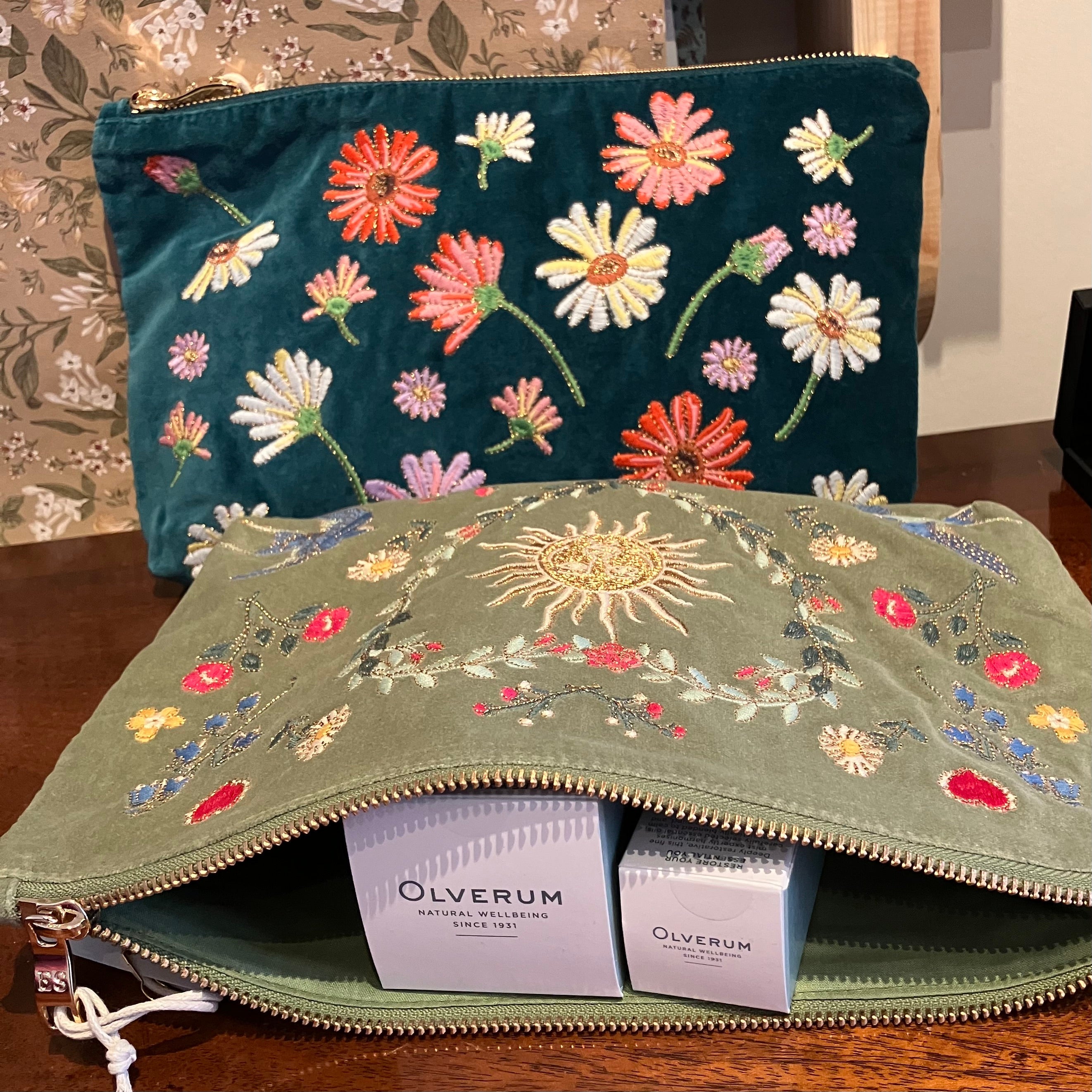 one-teal-velvet-pouch-with-embroidered-flowers-second-pale-green-velvet-pouch-with-floral-and-sun-embroidery-lying-open-with-two-olverum-boxes