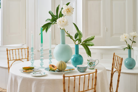 Dining room with white walls, wooden chairs, and a table set with plates, cutlery, and decorative vases.