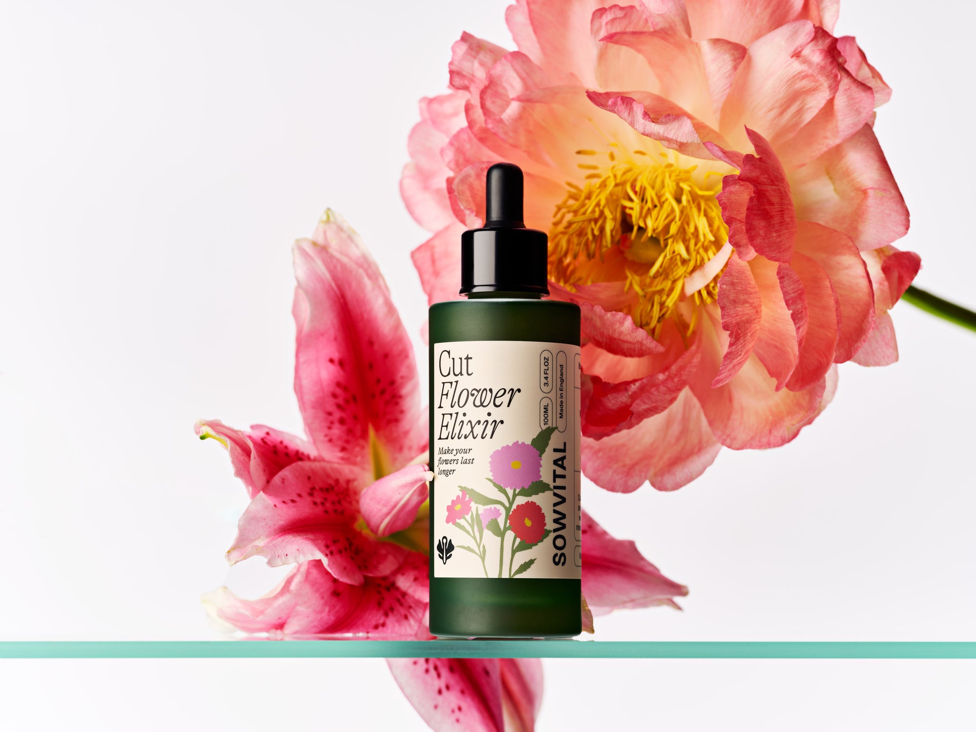 Bottle of Cut Flower Elixir with pink flowers in the background
