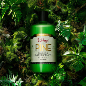 Green bottle of Wiberg's Pine Bath Essence surrounded by green leaves and plants