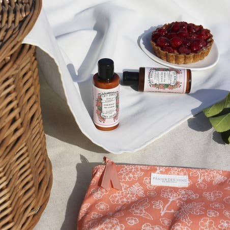 two skincare bottles with bag on white cloth with a fruit tart on plate and backet