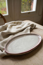 red-stripe-round-edge-0f-oval-plate-on-wooden-table-with-teatowel-window-in-background.