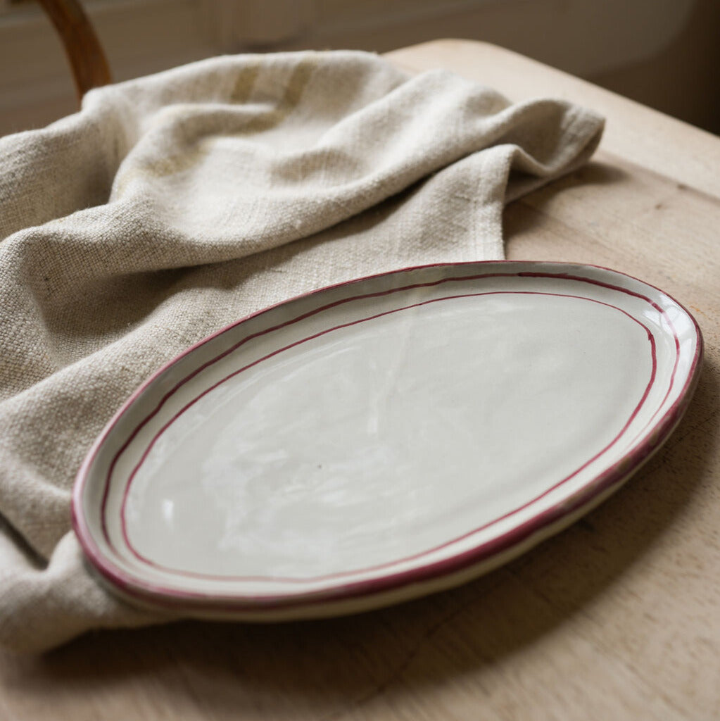 Oval-plate-edged-with-3-red-lines-on-wooden-table-with-teatowel
