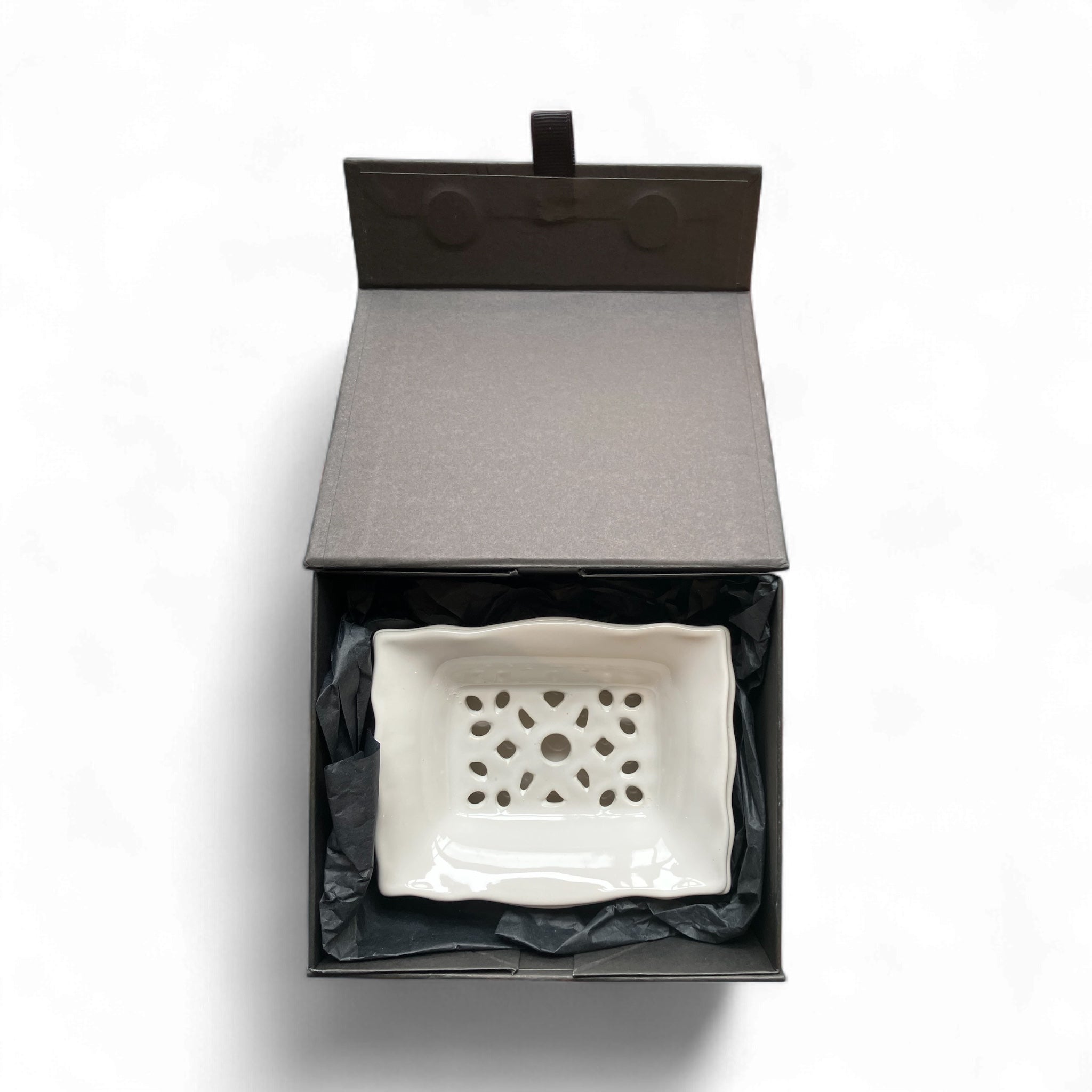 White ceramic dish with decorative pattern in an open black box on a white background