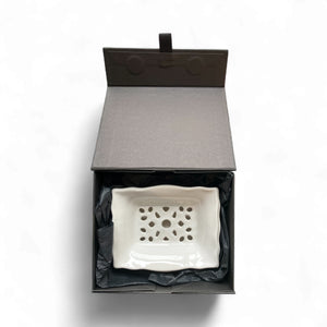 White ceramic dish with decorative pattern in an open black box on a white background